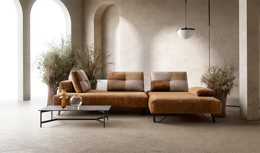 Divano modulare dal design contemporaneo, rivestito in tessuto caldo nei toni del marrone, con sedute ampie e linee essenziali, ideale per ambienti eleganti e luminosi.