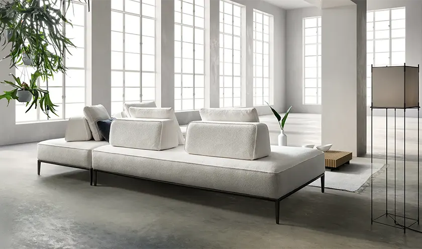 Divano modulare dal design contemporaneo, rivestito in tessuto nei toni del grigio chiaro, con sedute ampie e linee essenziali.