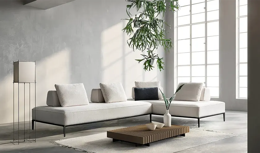 Divano modulare dal design contemporaneo, rivestito in tessuto nei toni del grigio chiaro, con sedute ampie e linee essenziali.