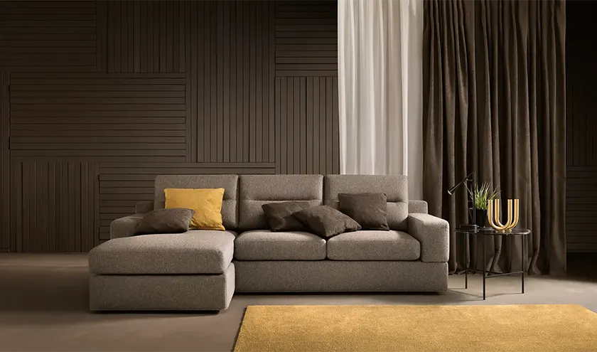 Divano angolare moderno con linee semplici, in tessuto grigio, abbinato a un tappeto giallo in un ambiente living elegante.