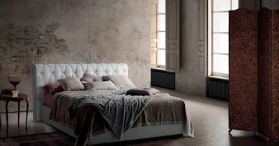 Interno di una camera da letto con un letto imbottito, un comodino e una parete stile industriale.